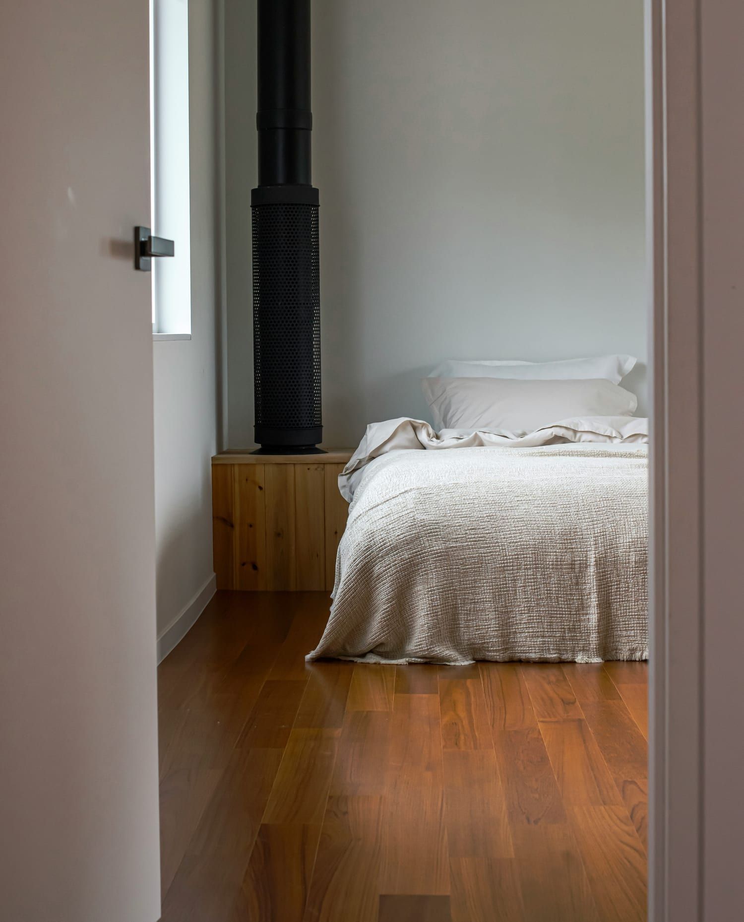 Chambre vue par une porte entrouverte, lit fait de linge clair sur un parquet
