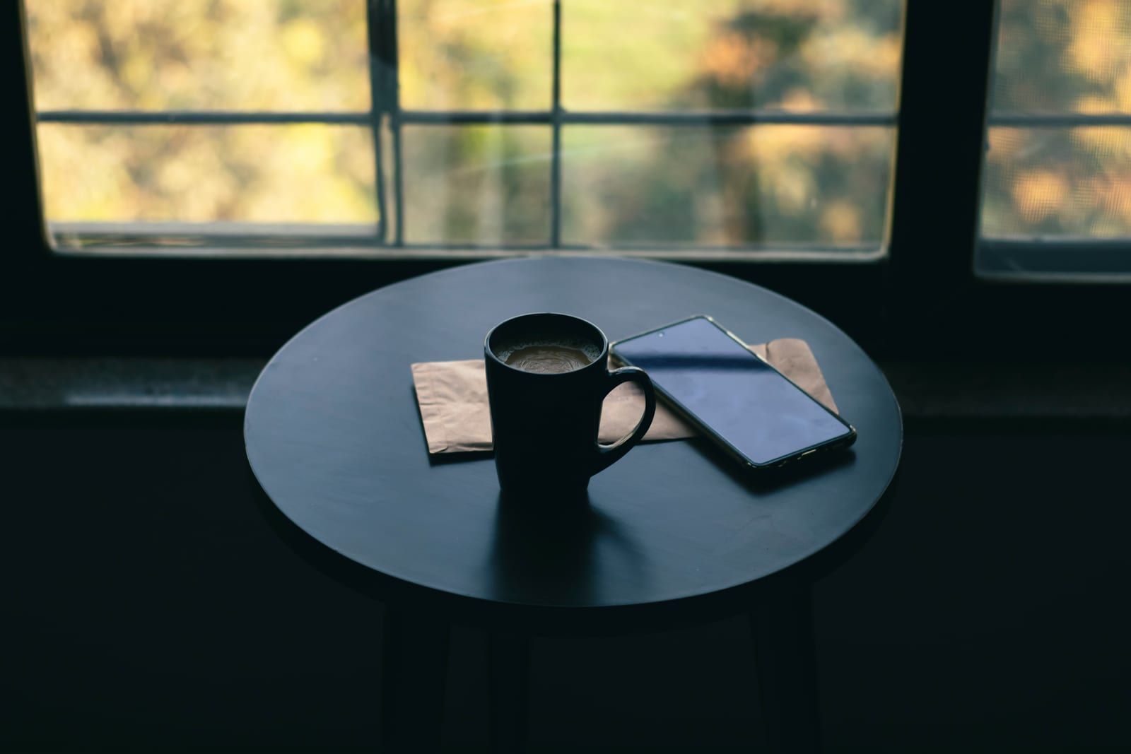 Tasse de café et téléphone posés sur une table ronde devant une fenêtre