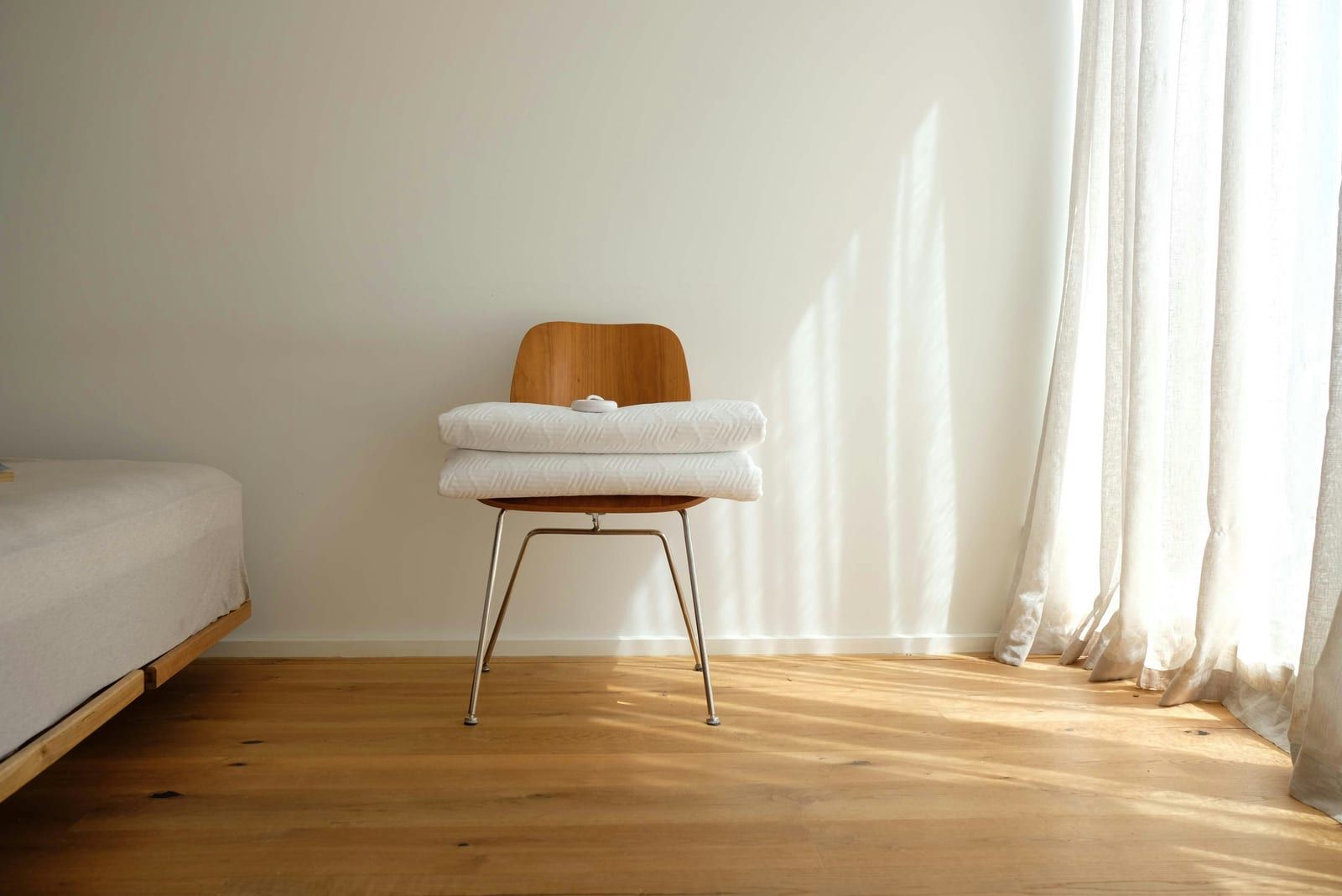 Serviettes blanches pliées sur une chaise en bois près d'un lit, voilage clair dans la lumière